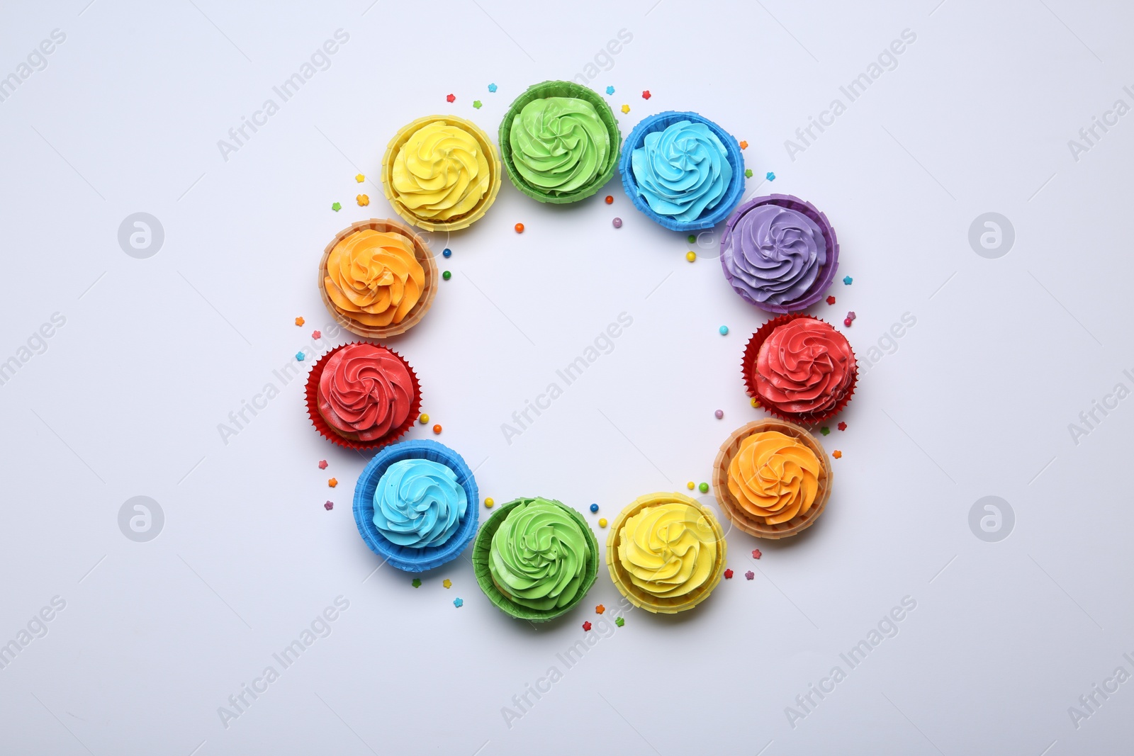 Photo of Frame of tasty cupcakes with bright cream and sprinkles on white background, flat lay. Space for text