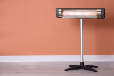 Modern electric infrared heater on floor in room, space for text