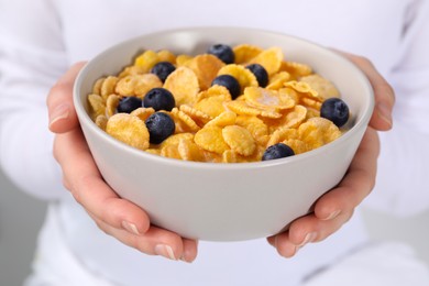 Woman holding bowl of crispy corn flakes with milk and blueberries, closeup