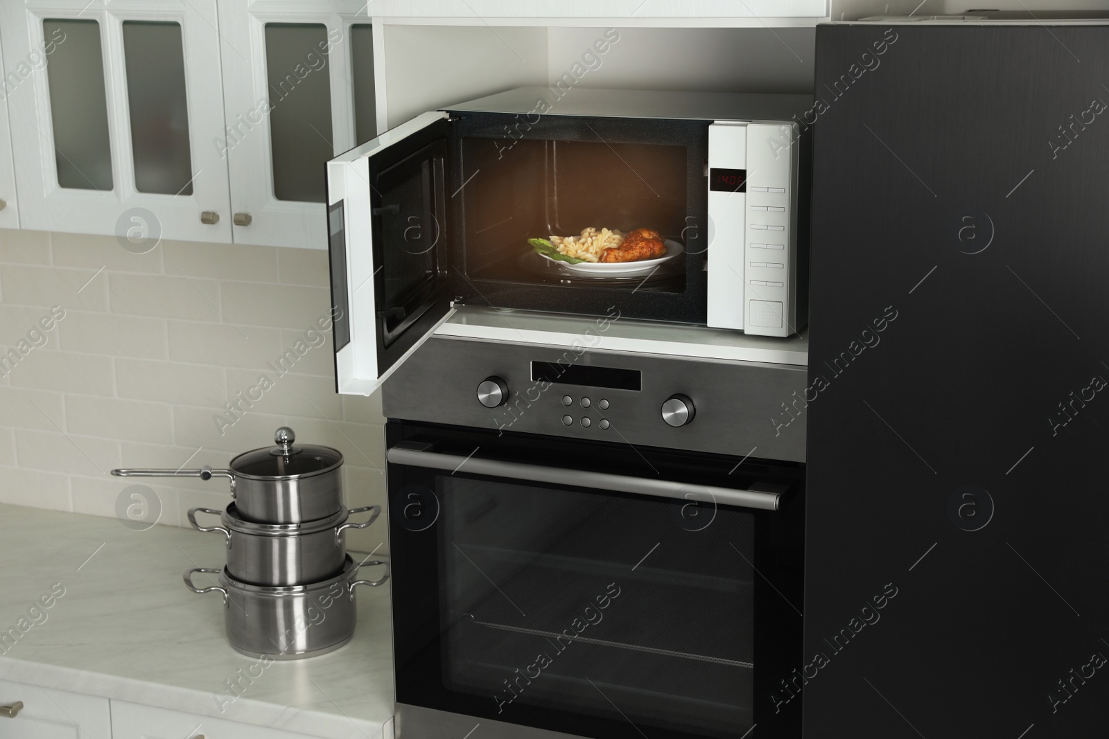 Photo of Open microwave oven with food on white shelf in kitchen