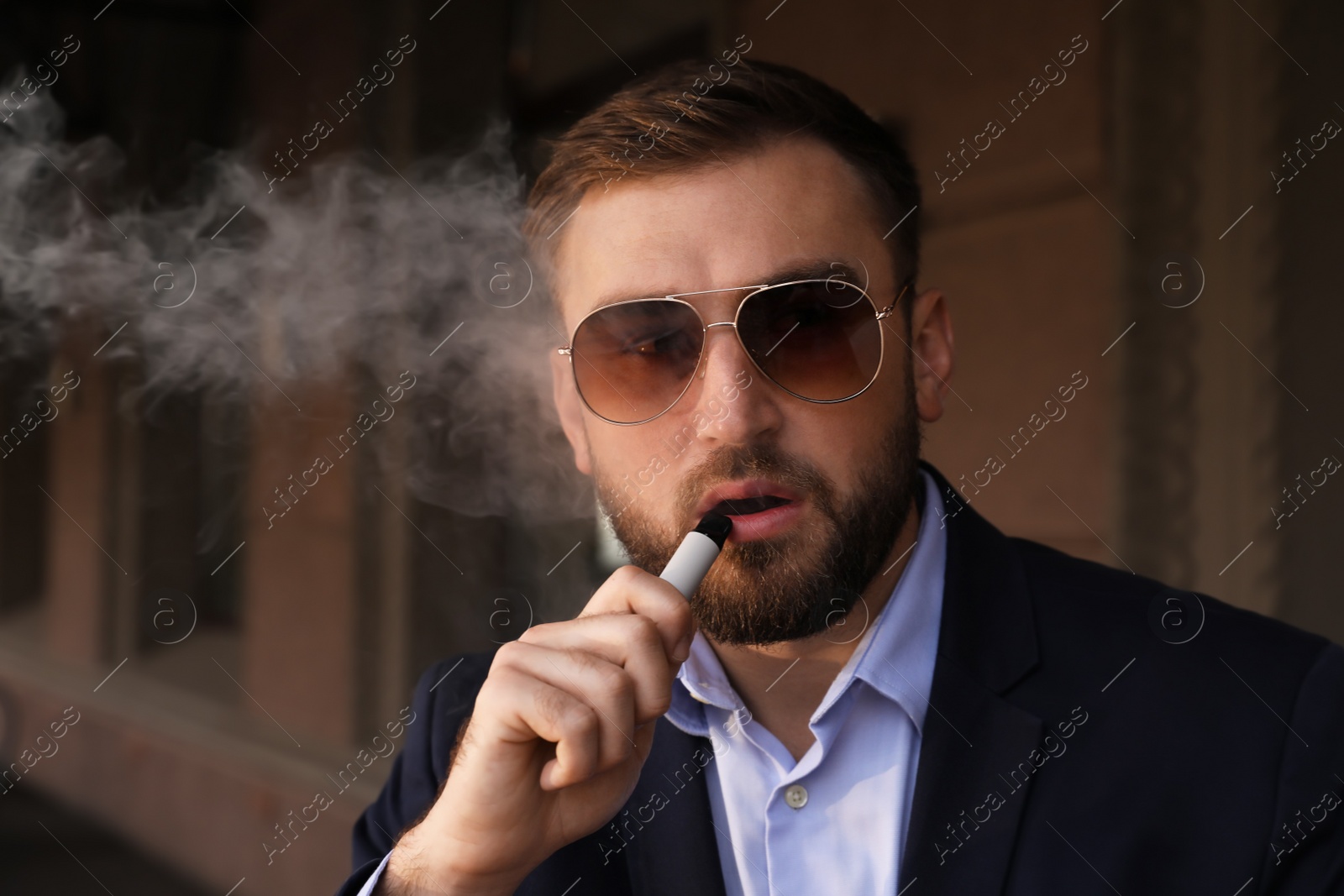 Photo of Handsome young businessman using disposable electronic cigarette outdoors