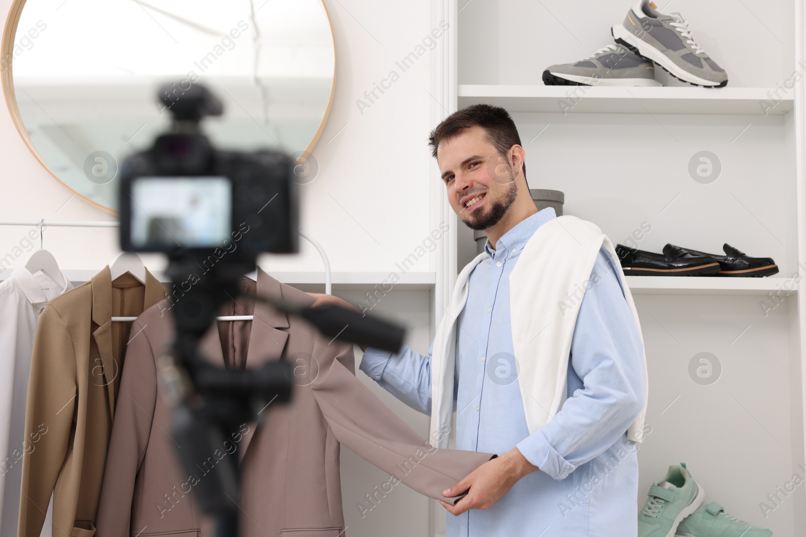 Photo of Smiling fashion blogger showing clothes while recording video at home