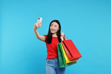 Photo of Smiling woman with shopping bags taking selfie on light blue background