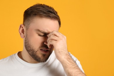 Man suffering from migraine on yellow background, space for text