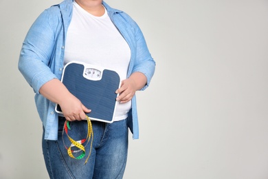 Overweight woman with scales and measuring tape on light background