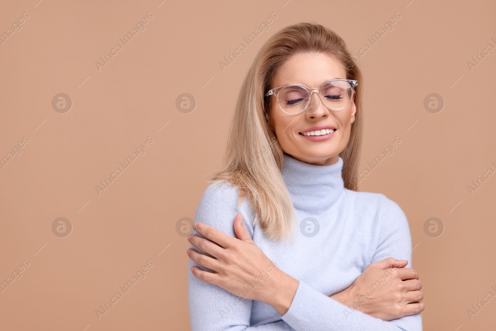 Photo of Portrait of smiling middle aged woman in glasses with crossed arms on beige background. Space for text