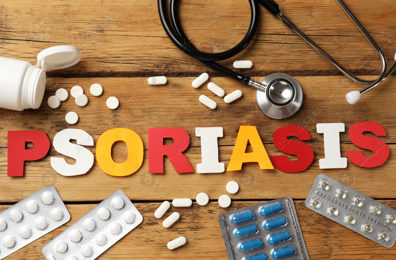 Photo of Word Psoriasis made of paper letters, stethoscope and pills on wooden table, flat lay