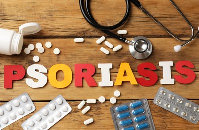 Word Psoriasis made of paper letters, stethoscope and pills on wooden table, flat lay