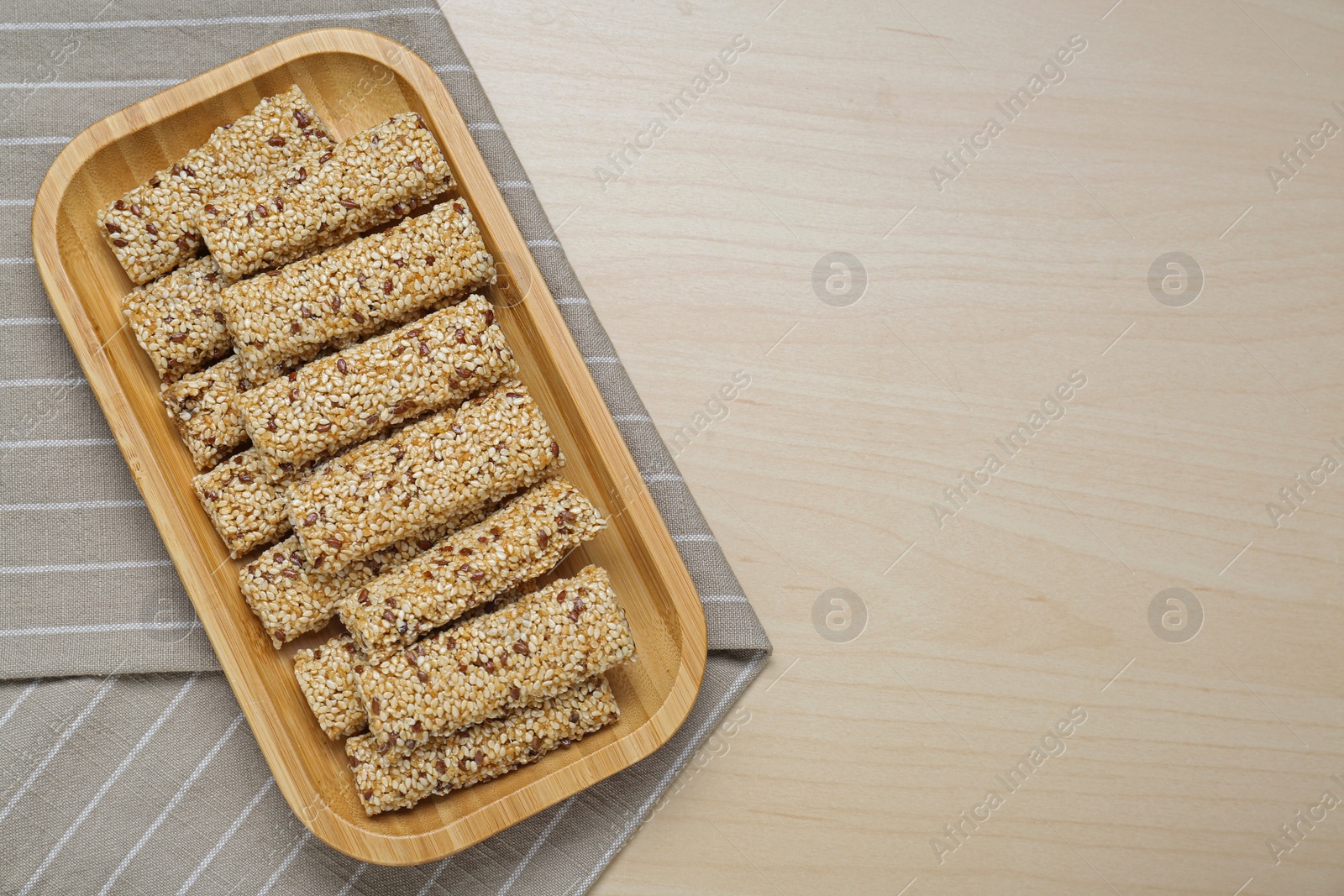 Photo of Plate with tasty sesame seed bars on wooden table, top view. Space for text