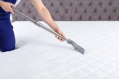 Photo of Man disinfecting mattress with vacuum cleaner, closeup. Space for text