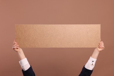 Woman holding blank cardboard banner on brown background, closeup. Space for text
