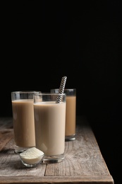 Glasses with protein shakes and powder in bowl on table against black background