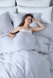 Photo of Young woman awaking in comfortable bed with silky linens, above view