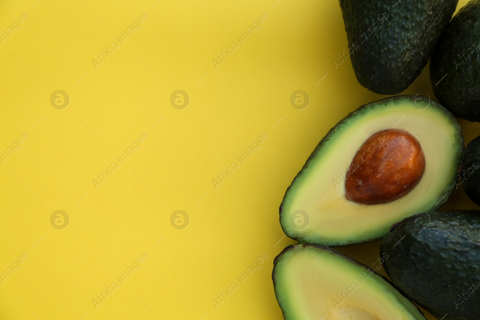 Photo of Fresh whole and cut avocados on yellow background, flat lay. Space for text