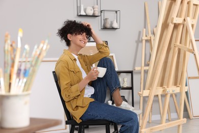 Photo of Young woman with cup near easel in studio