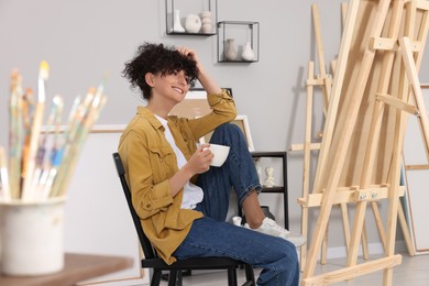 Young woman with cup near easel in studio