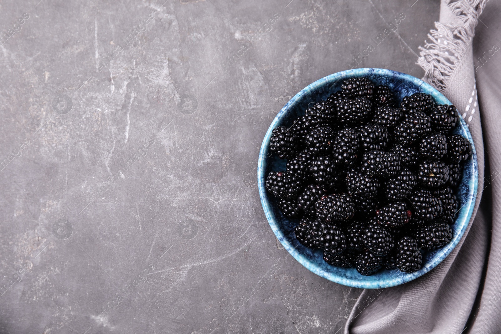 Photo of Bowl of ripe blackberries and fabric on grey table, flat lay with space for text