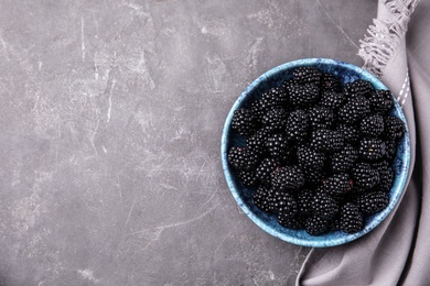 Photo of Bowl of ripe blackberries and fabric on grey table, flat lay with space for text