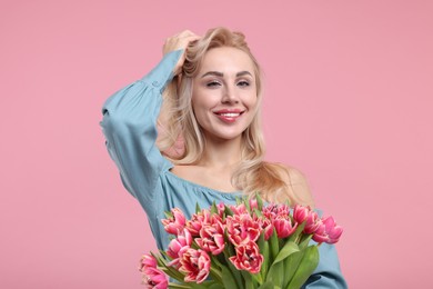 Happy young woman with beautiful bouquet on dusty pink background