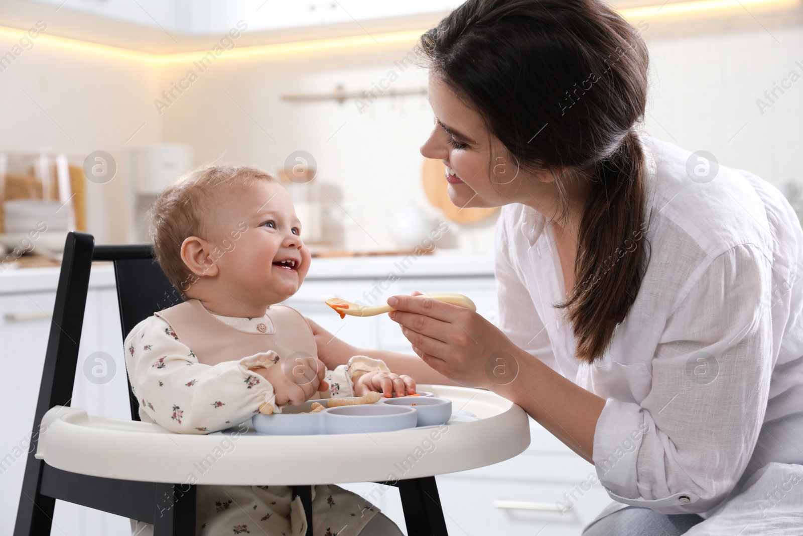 Photo of Mother feeding her cute little baby in kitchen