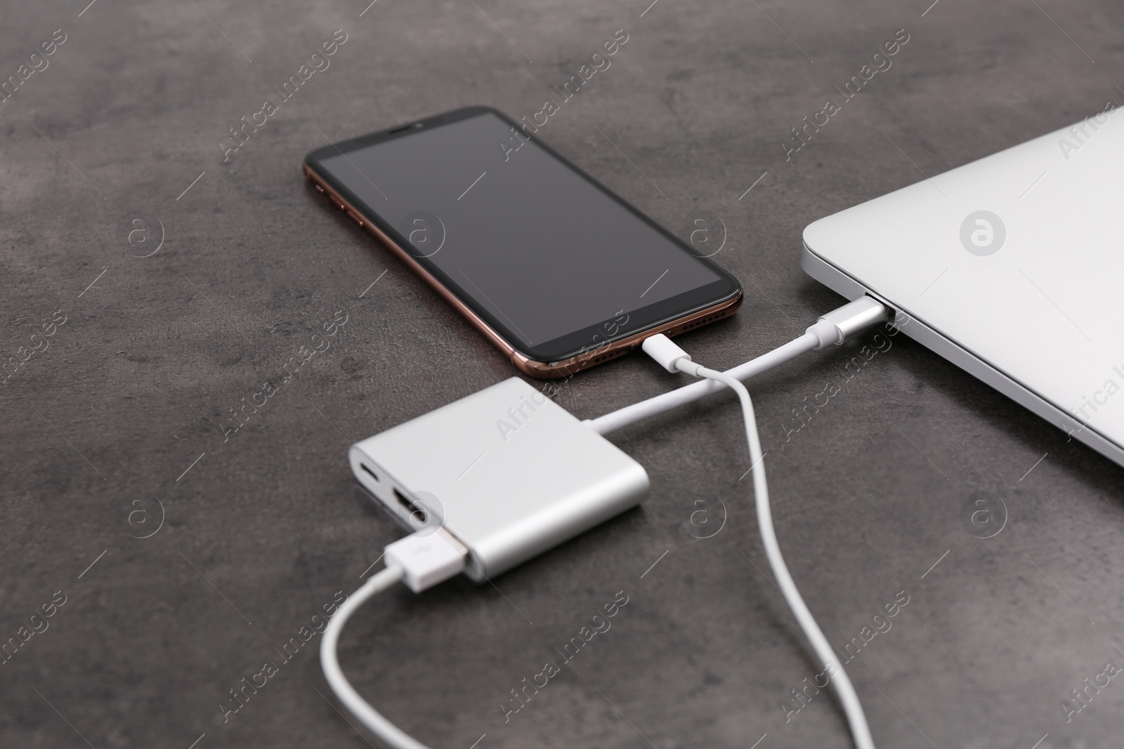 Photo of Modern smartphone and laptop charging from power bank on grey table, closeup