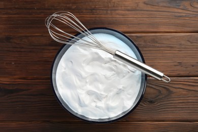 Photo of Bowl with whipped cream and whisk on wooden table, top view