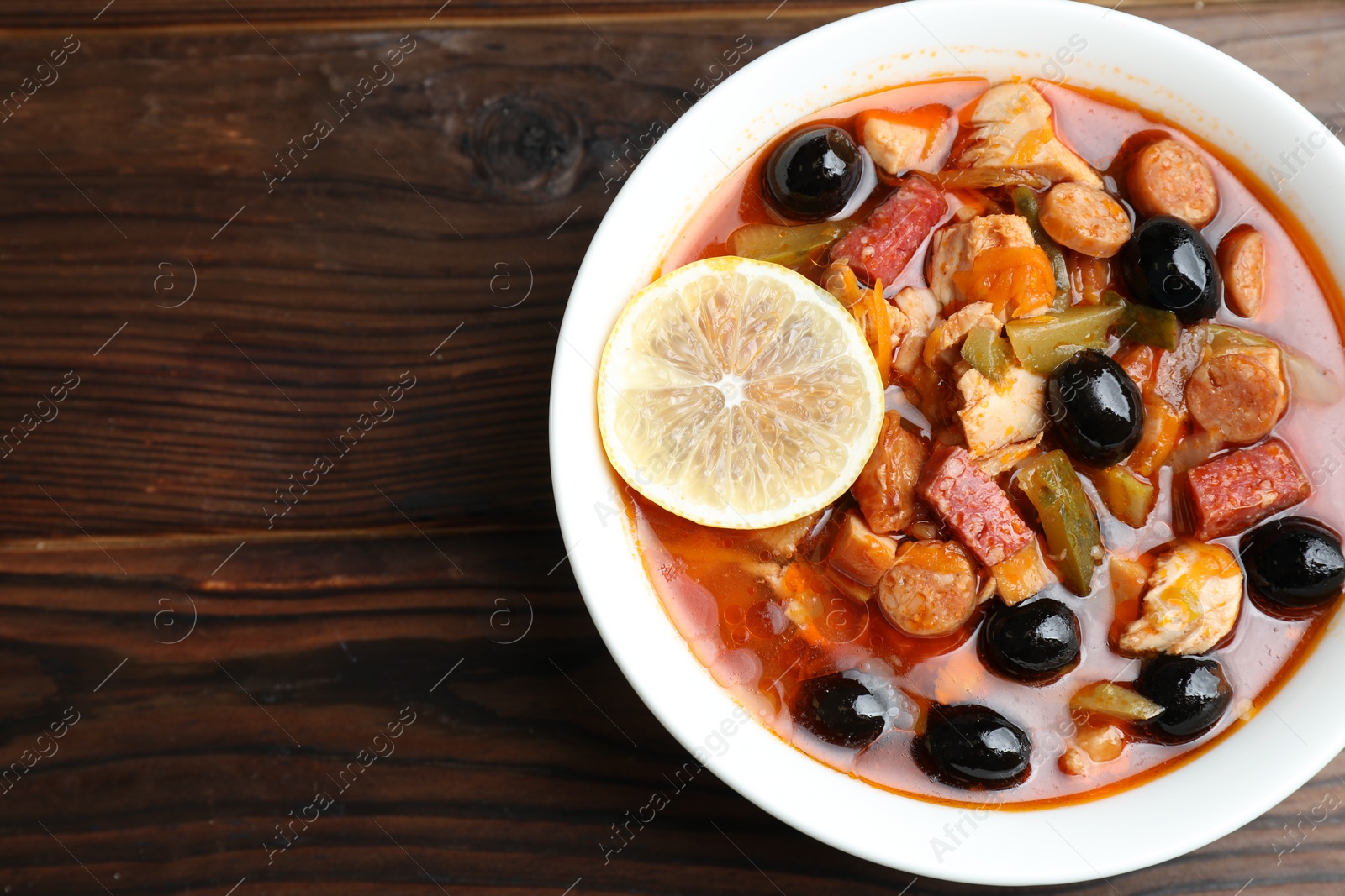 Photo of Meat solyanka soup with sausages, olives and vegetables on wooden table, top view. Space for text