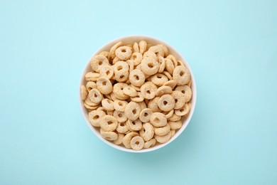 Photo of Tasty cereal rings in bowl on light blue table, top view