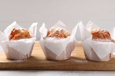 Photo of Delicious muffins with powdered sugar on light table, closeup