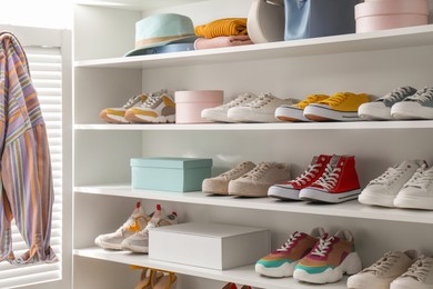 Photo of White shelving unit with collection of colorful sneakers and accessories indoors