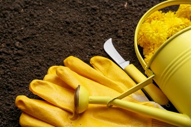 Photo of Gardening tools, gloves and flowers on fresh soil, closeup