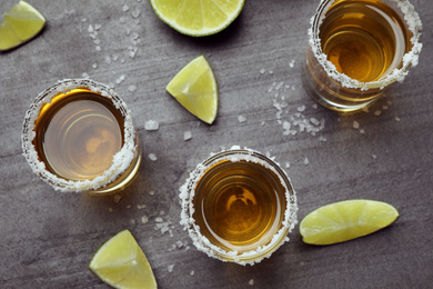 Mexican Tequila shots, lime slices and salt on grey table, flat lay