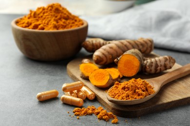 Photo of Aromatic turmeric powder, pills and raw roots on grey table