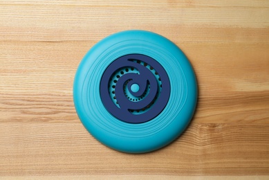 Photo of Blue plastic frisbee disk on wooden background, top view