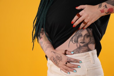 Young woman with tattoos on body against yellow background, closeup
