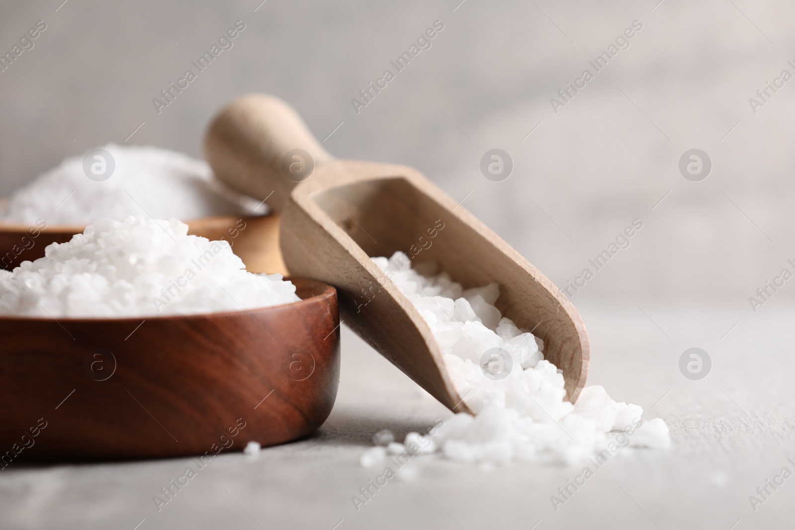 Photo of Natural salt in bowls and scoop on grey table, closeup