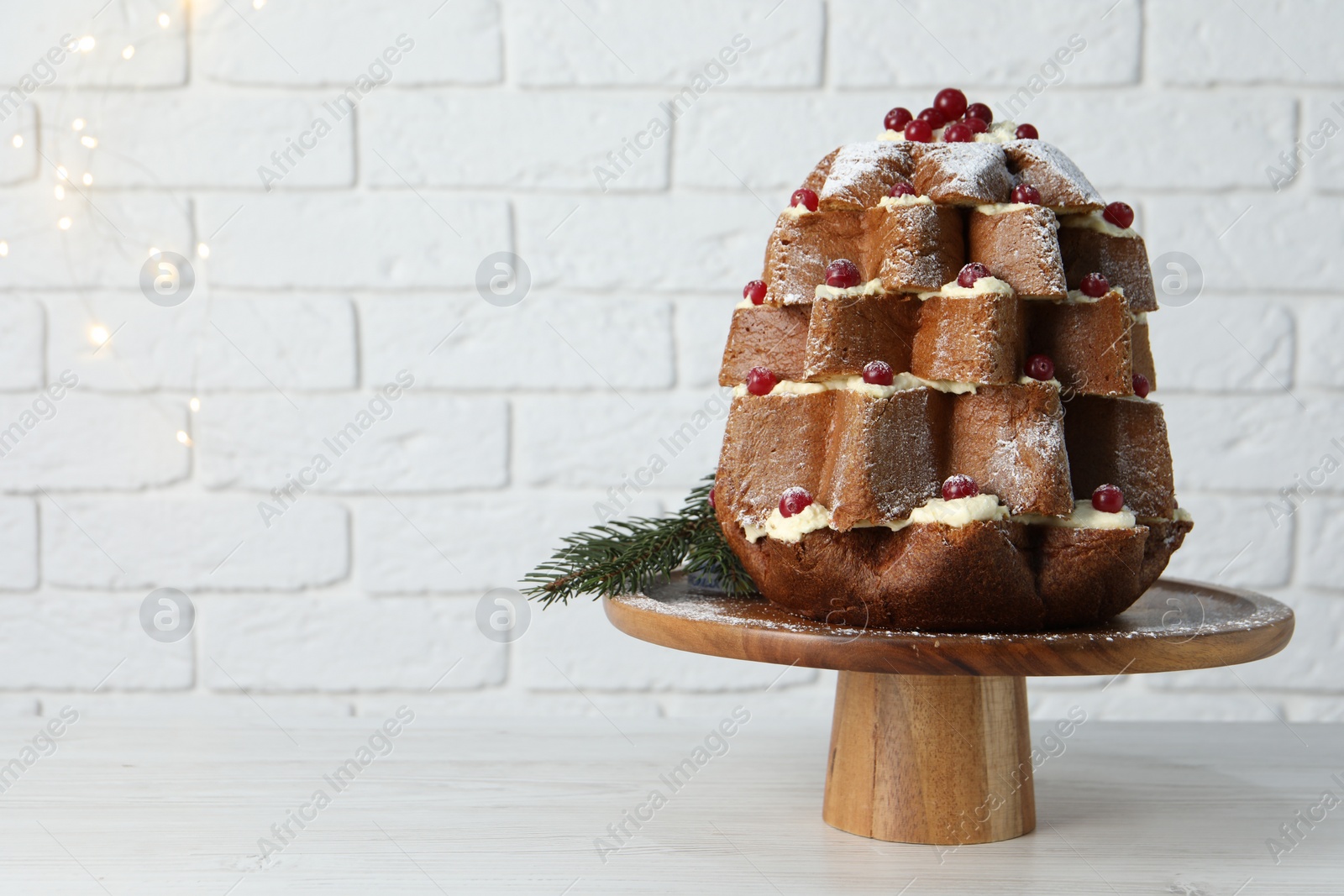 Photo of Delicious Pandoro Christmas tree cake with powdered sugar and berries on white table near brick wall. Space for text
