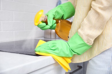 Photo of Woman cleaning induction cooktop with rag and detergent indoors, closeup