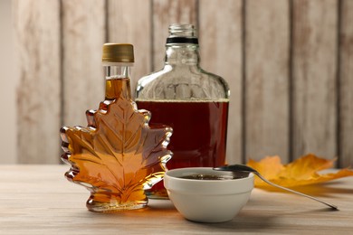 Photo of Bottles and bowl of tasty maple syrup on wooden table