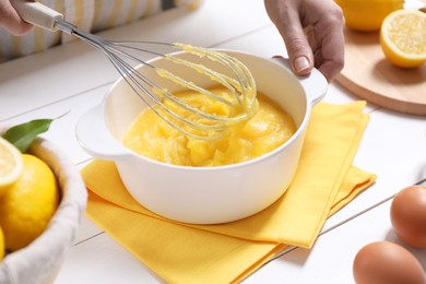 Photo of Woman cooking lemon curd at white wooden table, closeup