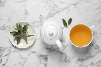 Photo of Cup of sage tea, green leaves and teapot on white marble table, flat lay