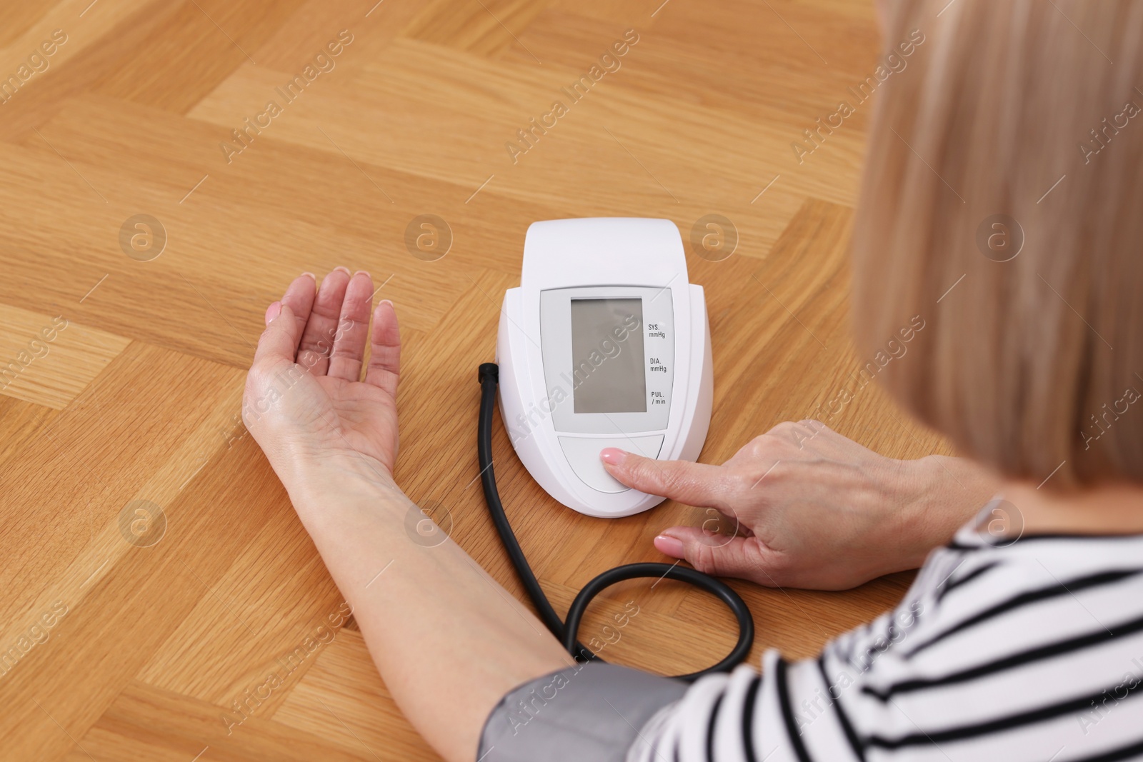 Photo of Woman measuring her blood pressure with tonometer at wooden table indoors, closeup