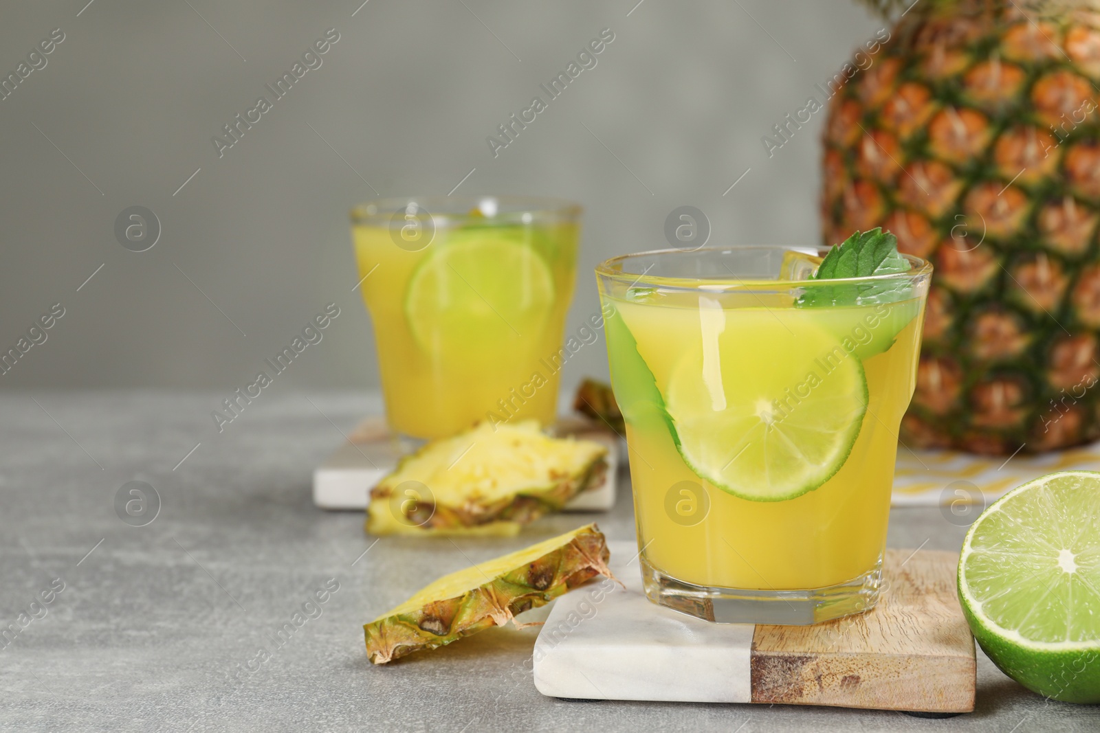 Photo of Glasses of tasty pineapple cocktail with mint and lime on light grey table. Space for text