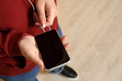 Man plugging headphones to smartphone indoors, closeup. Space for text