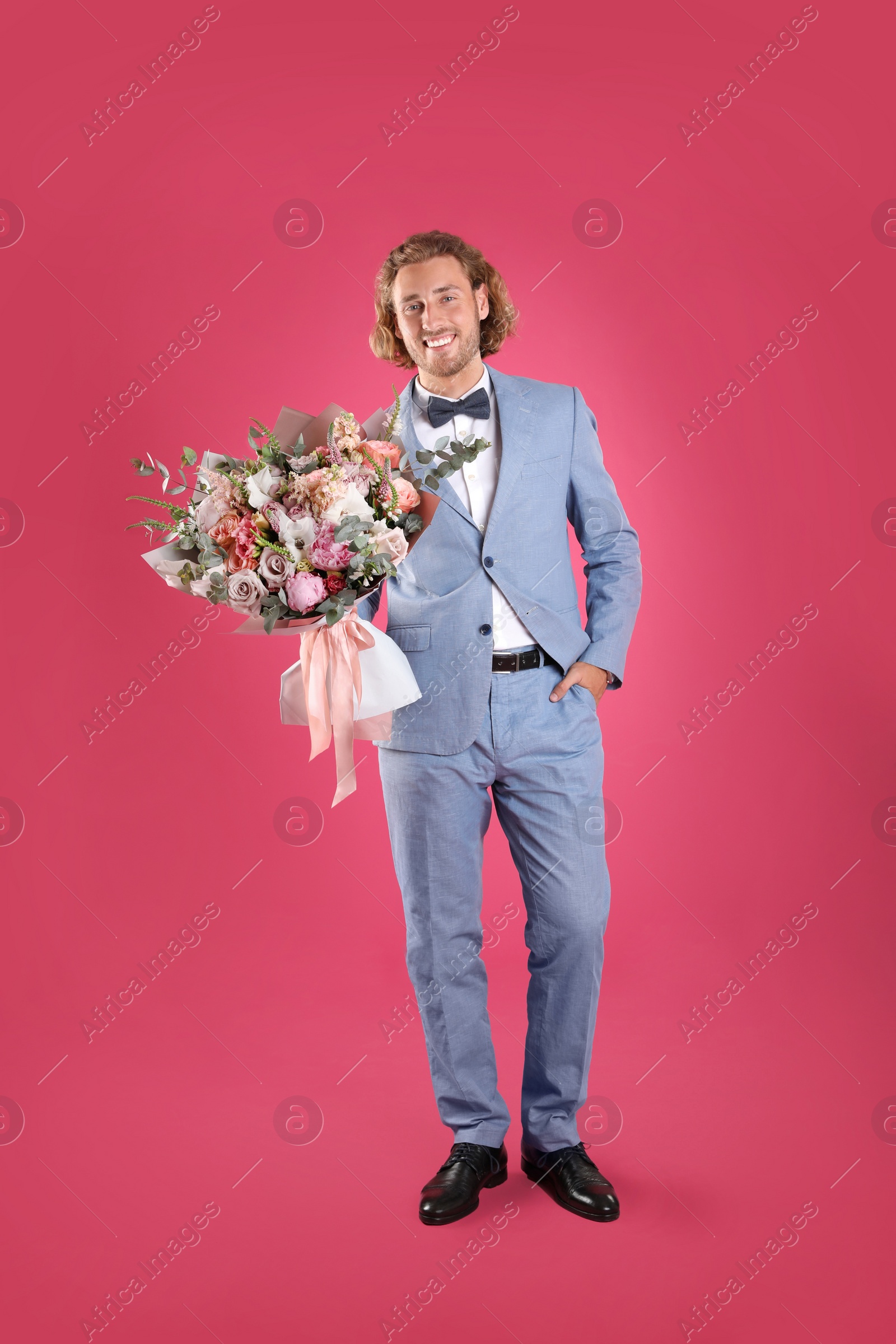 Photo of Young handsome man in stylish suit with beautiful flower bouquet on pink background