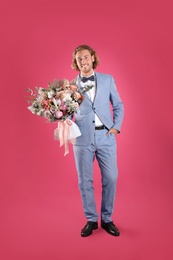 Photo of Young handsome man in stylish suit with beautiful flower bouquet on pink background