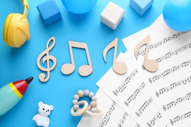 Photo of Baby songs. Music sheets, wooden notes, different toys and headphones on light blue background, flat lay