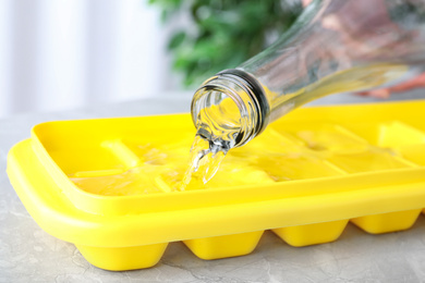 Photo of Pouring water into ice cube tray on table, closeup