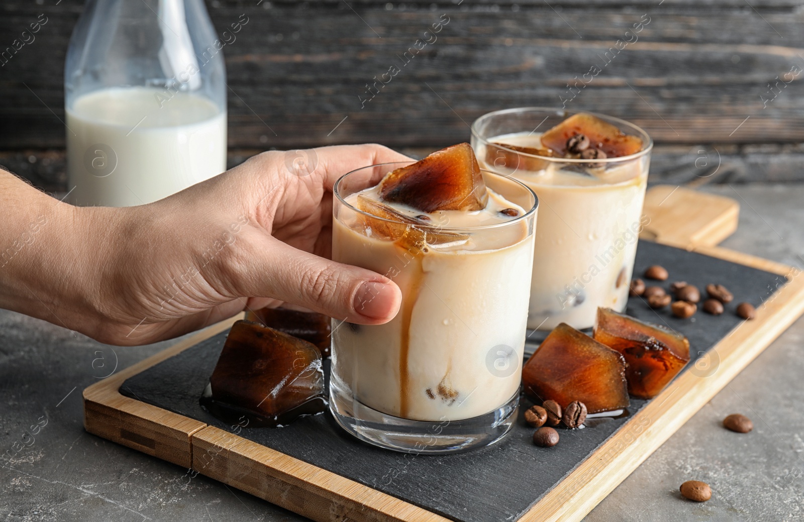 Photo of Woman taking glass of milk with coffee ice cubes from board on table