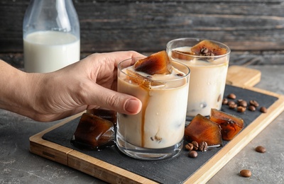 Woman taking glass of milk with coffee ice cubes from board on table